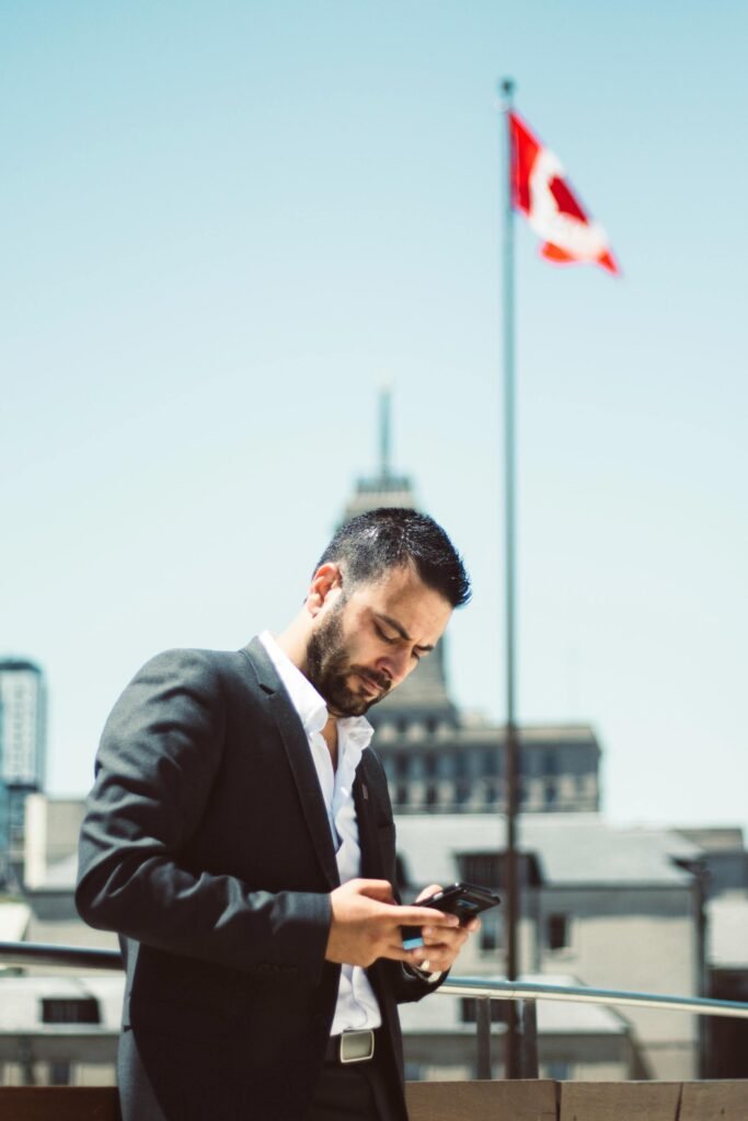 Businessman standing outdoors, using phone with Canadian flag in the background.